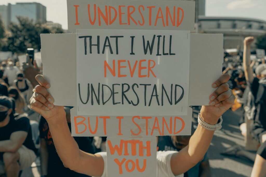 A protester holds up a sign that reads, "I understand that I will never understand, but I stand with you." The would could stand to hear this message daily.
